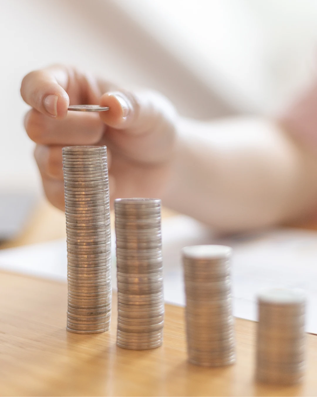 Mano apilando monedas en columnas que ilustran métodos sobre cómo ahorrar siendo joven