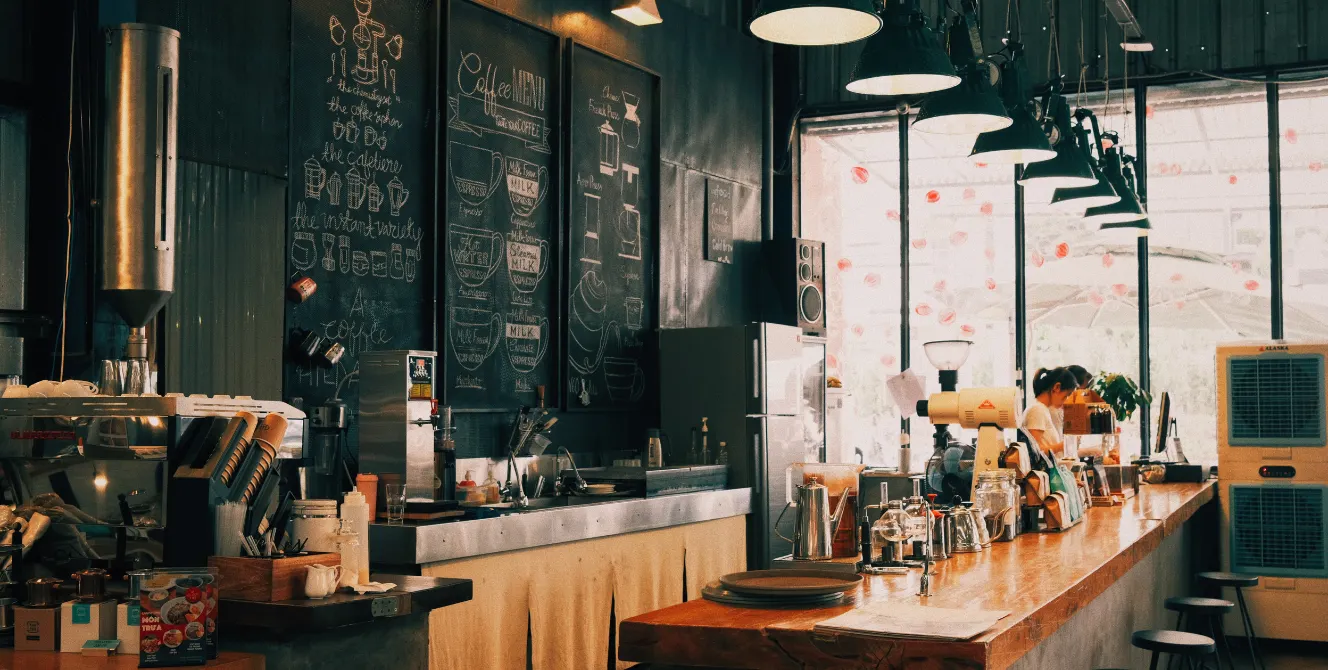 Interior de un bar moderno con barra de madera y baristas preparando café, ideal para ilustrar las coberturas de un seguro para bares.