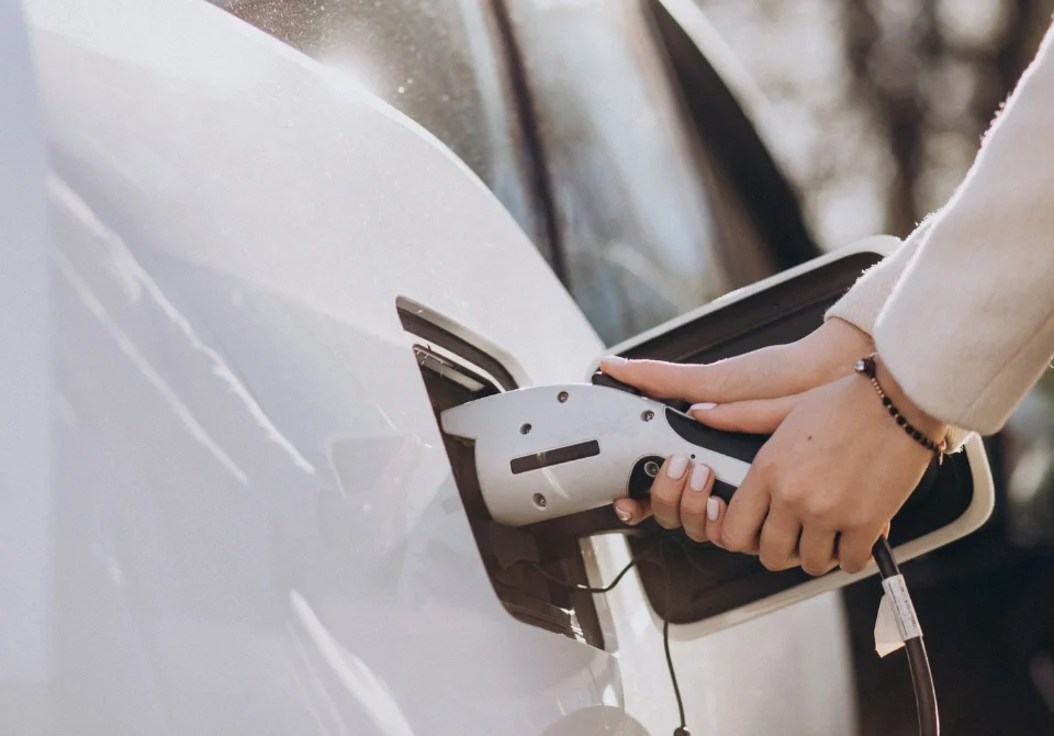 Mujer cargando un coche eléctrico en una estación de carga, imagen que representa la movilidad sostenible y la importancia de contar con un seguro coche electrico adaptado a las nuevas necesidades de los conductores.