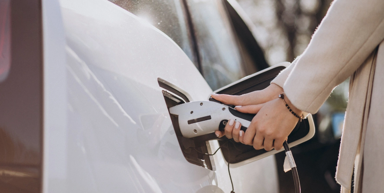 Mujer cargando un coche eléctrico en una estación de carga, imagen que representa la movilidad sostenible y la importancia de contar con un seguro coche electrico adaptado a las nuevas necesidades de los conductores.
