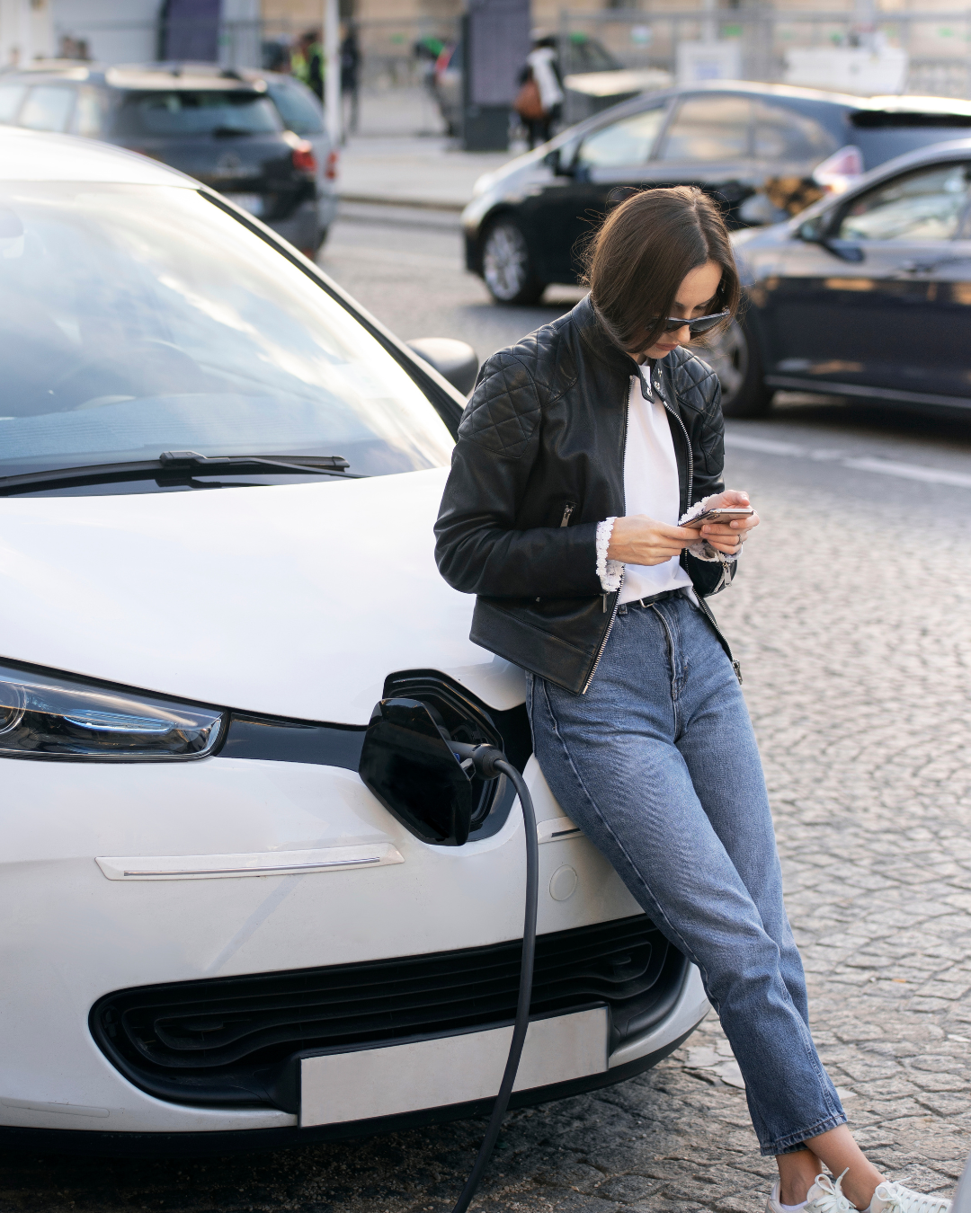 Mujer apoyada en un coche eléctrico mientras carga la batería, imagen que representa la movilidad sostenible y la protección que ofrece un seguro coche electrico adaptado a las nuevas necesidades de los conductores.