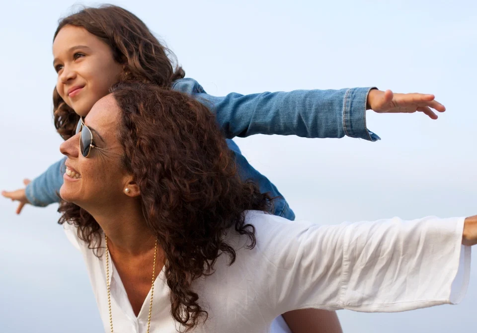 Madre con su hija a hombros al aire libre, imagen asociada a beneficiarios seguro vida y protección familiar.