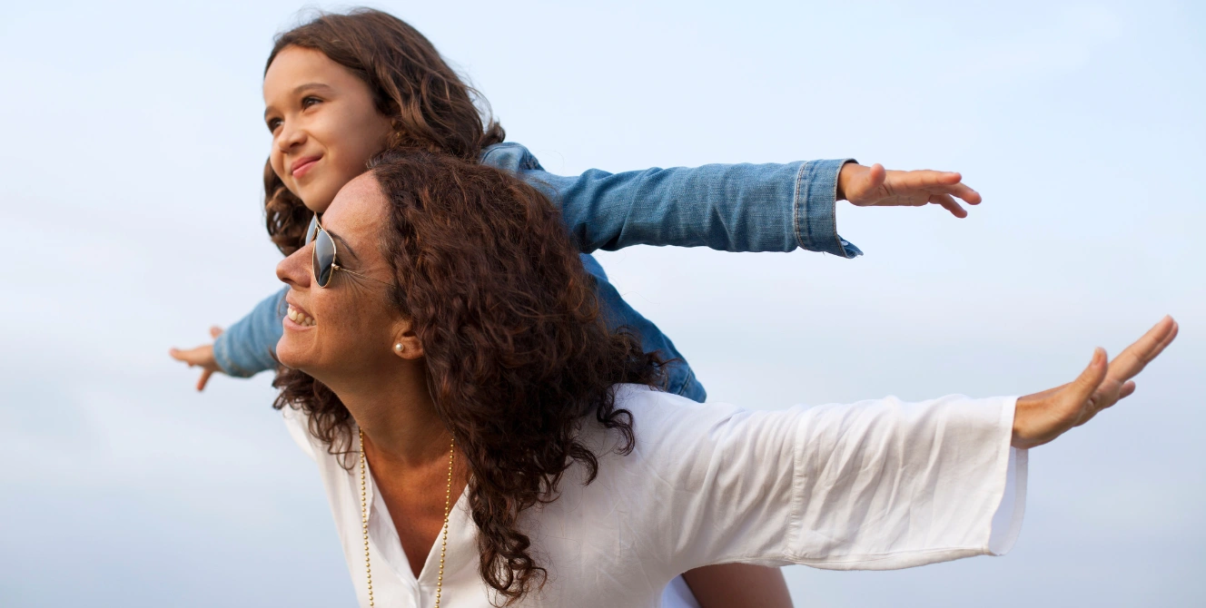 Madre con su hija a hombros al aire libre, imagen asociada a beneficiarios seguro vida y protección familiar.