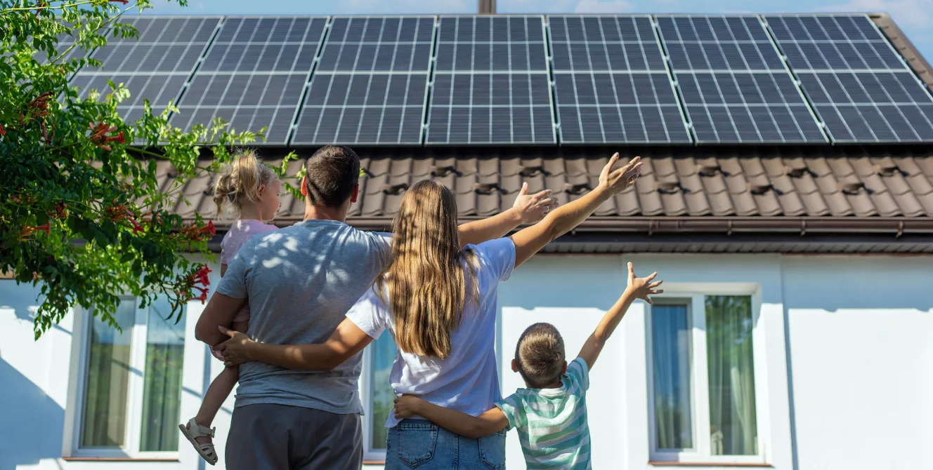 Familia con dos hijos contemplando su casa con placas solares en el tejado, símbolo de la inversión que protege un seguro para placas solares.